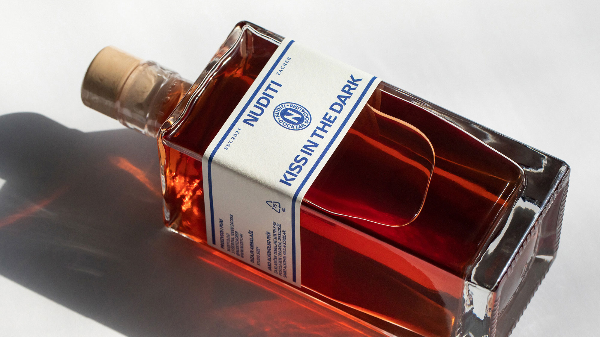 Lying bottle with brown liquid and the label: Nuditi Kiss in the Dark