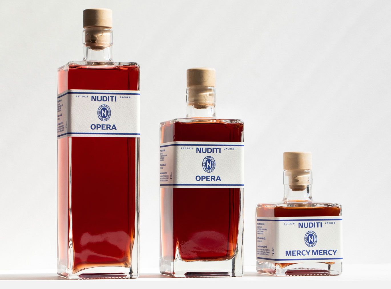 Three bottles with a brown liquid - two of them with the label: Nuditi Opera, one with the label: Nuditi Merci Merci